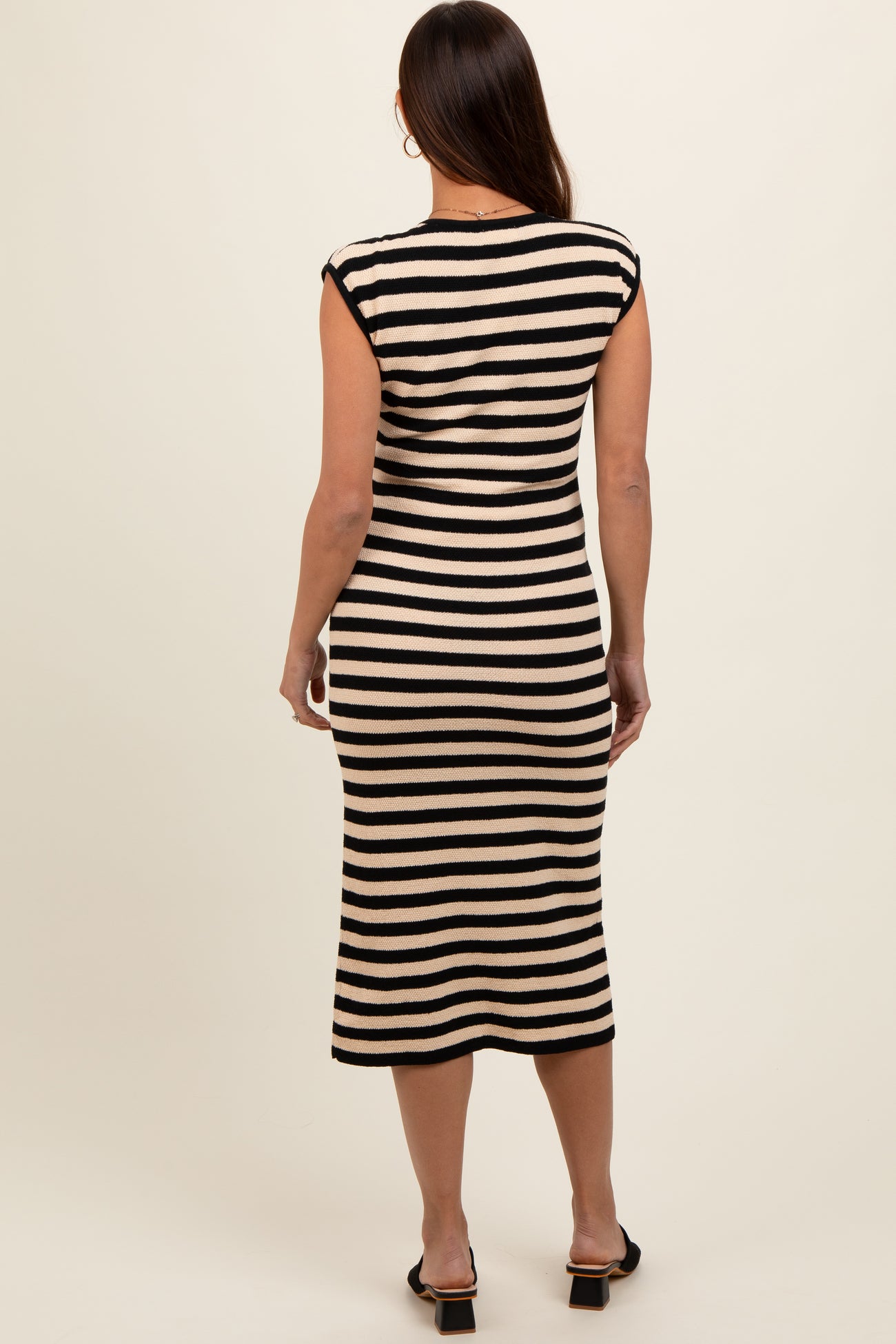 woman wearing a striped black and cream maternity midi dress, showing a fitted style and cap sleeves from the back