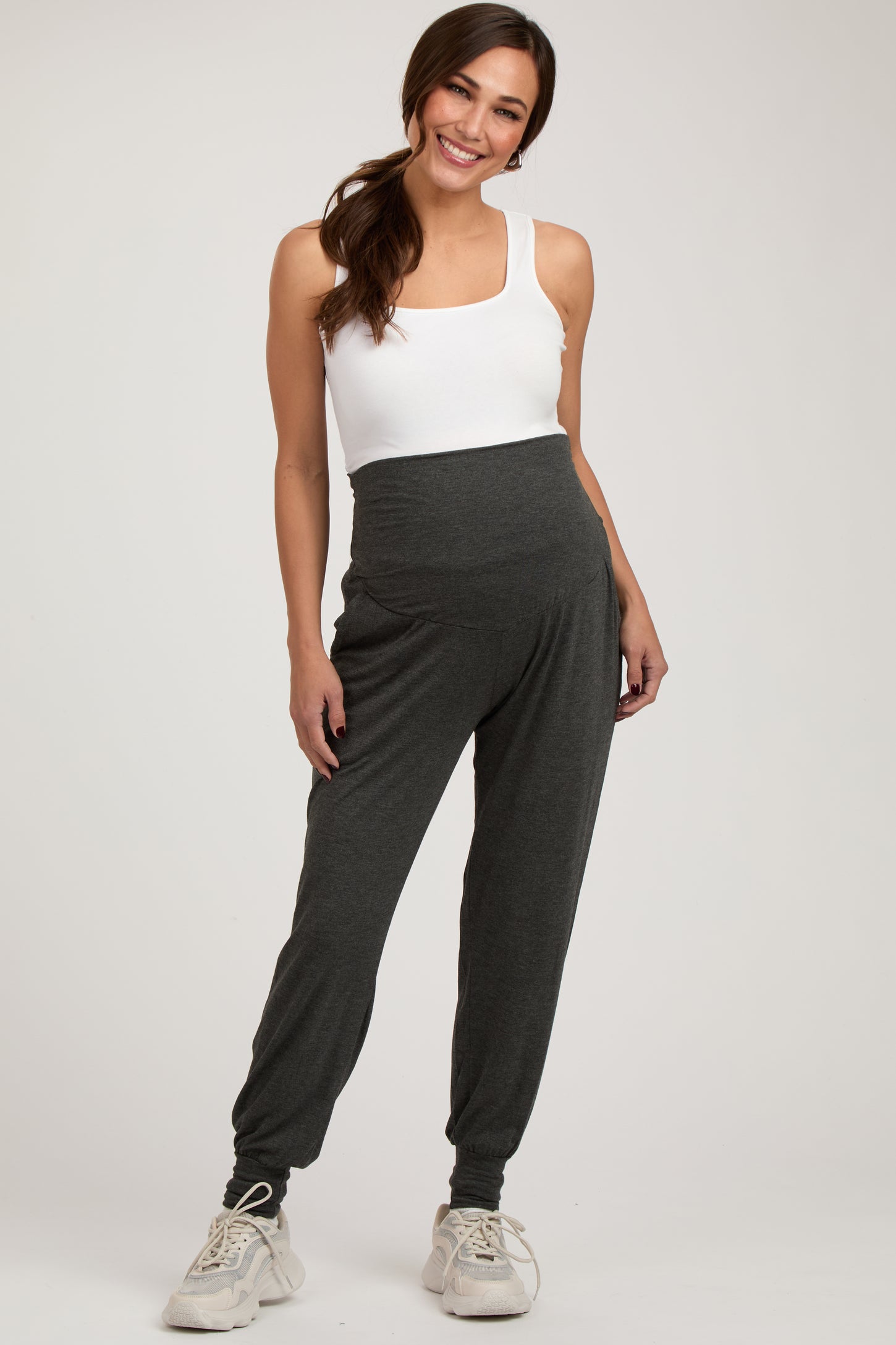 woman wearing a white tank top and dark gray maternity joggers with a supportive waist panel and side pockets