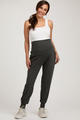woman wearing a white tank top and dark gray maternity joggers with a supportive waist panel and side pockets