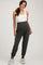 woman wearing a white tank top and dark gray maternity joggers with a supportive waist panel and side pockets