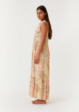woman wearing a sleeveless floral maxi dress with a tiered skirt and ruffled neckline standing sideways