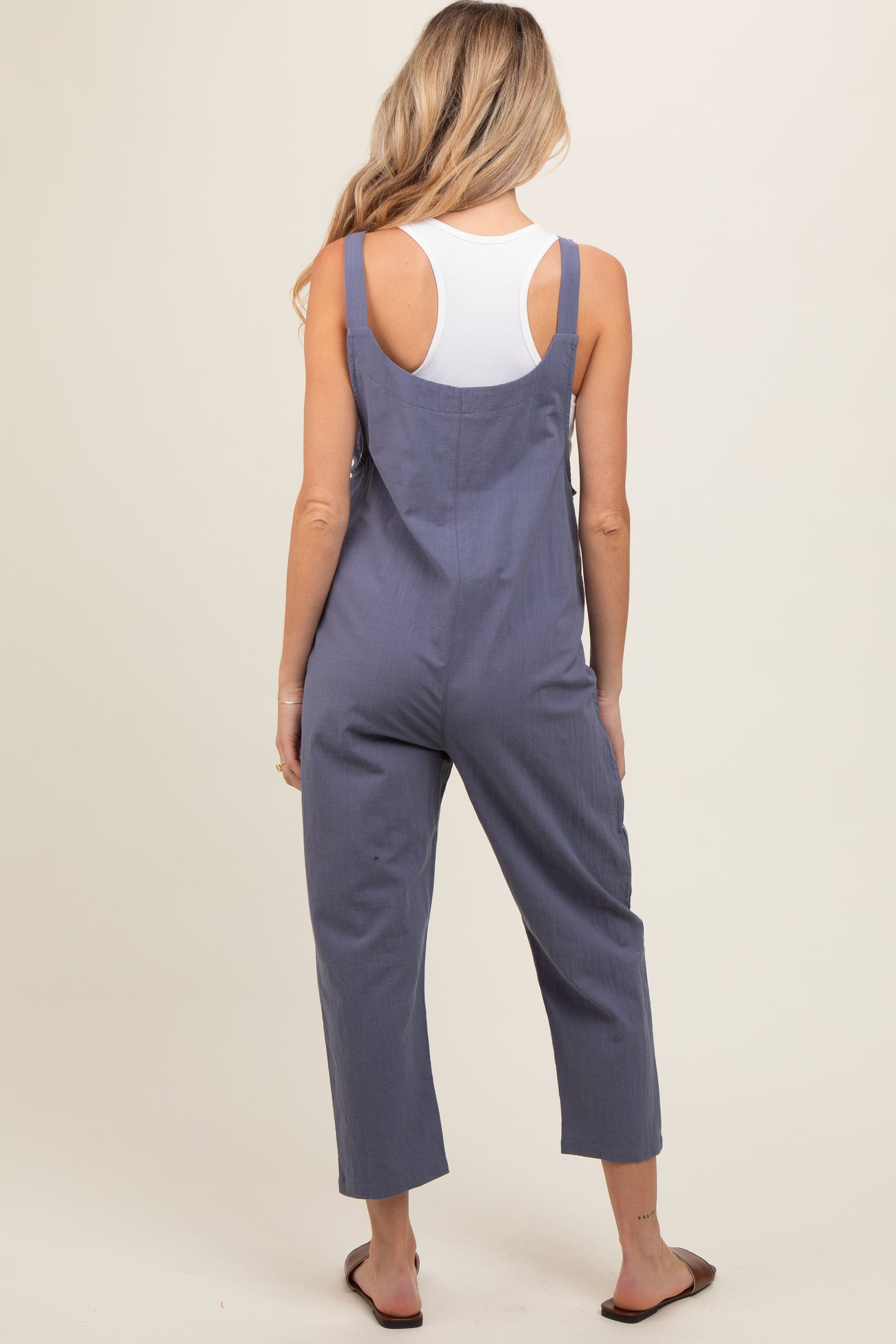 woman wearing a navy blue maternity jumpsuit with cropped legs and adjustable straps, seen from the back