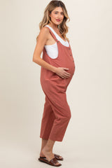 woman wearing a rust-colored maternity jumpsuit with buttons and a visible baby bump