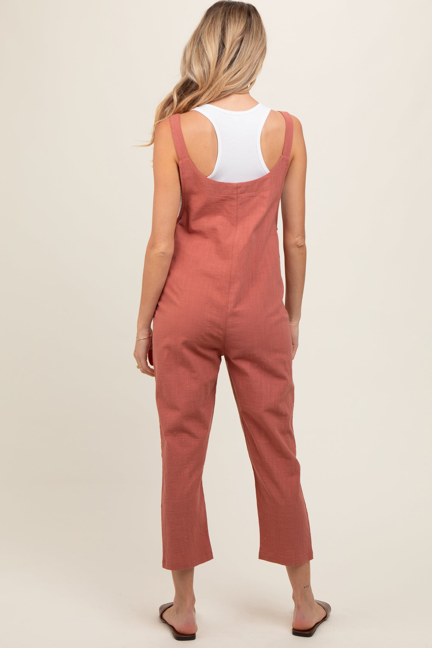 woman wearing a rust-colored maternity jumpsuit with wide legs and adjustable straps, shown from the back