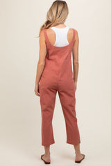 woman wearing a rust-colored maternity jumpsuit with wide legs and adjustable straps, shown from the back