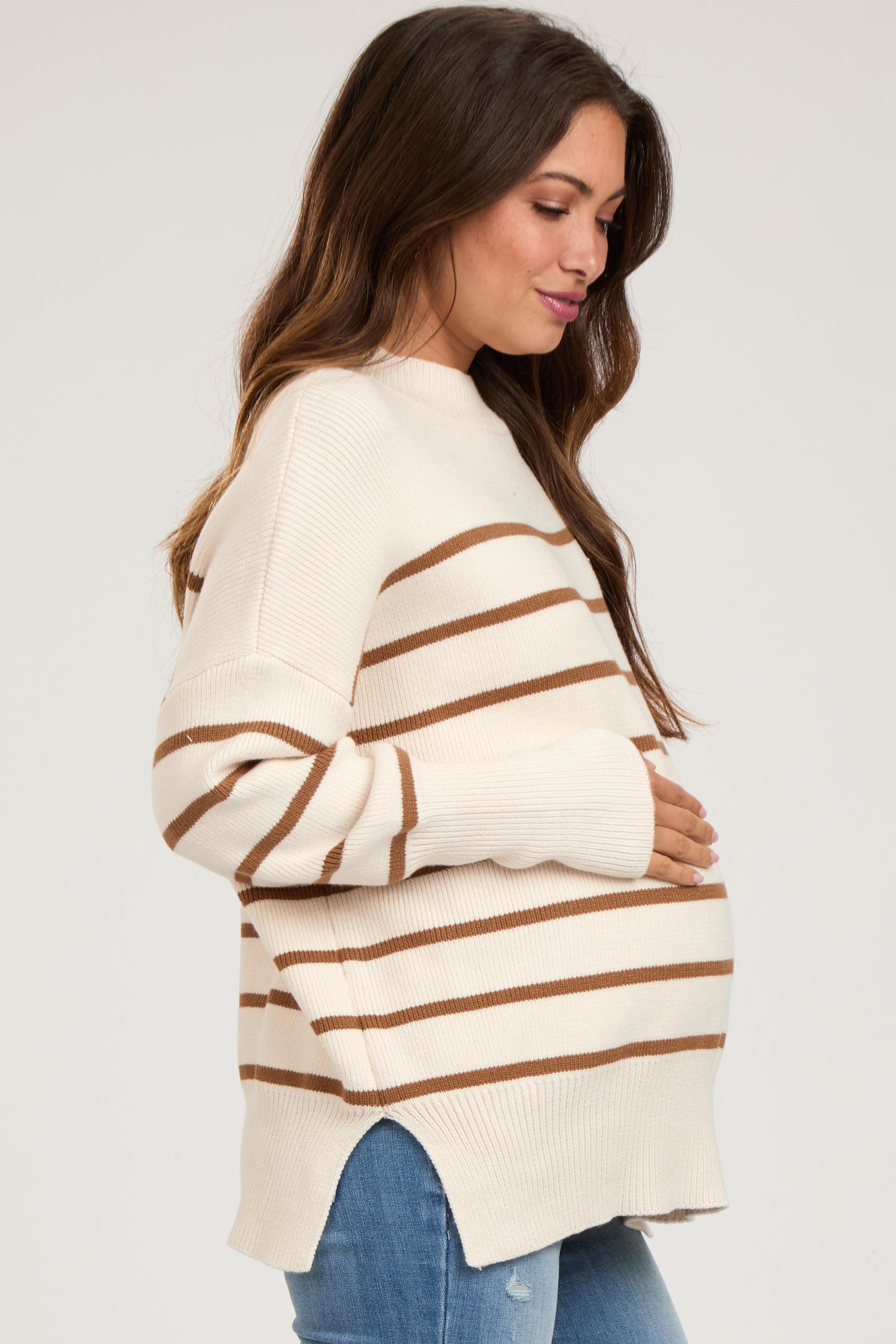 woman wearing a cream and brown striped maternity sweater, gently cradling her baby bump