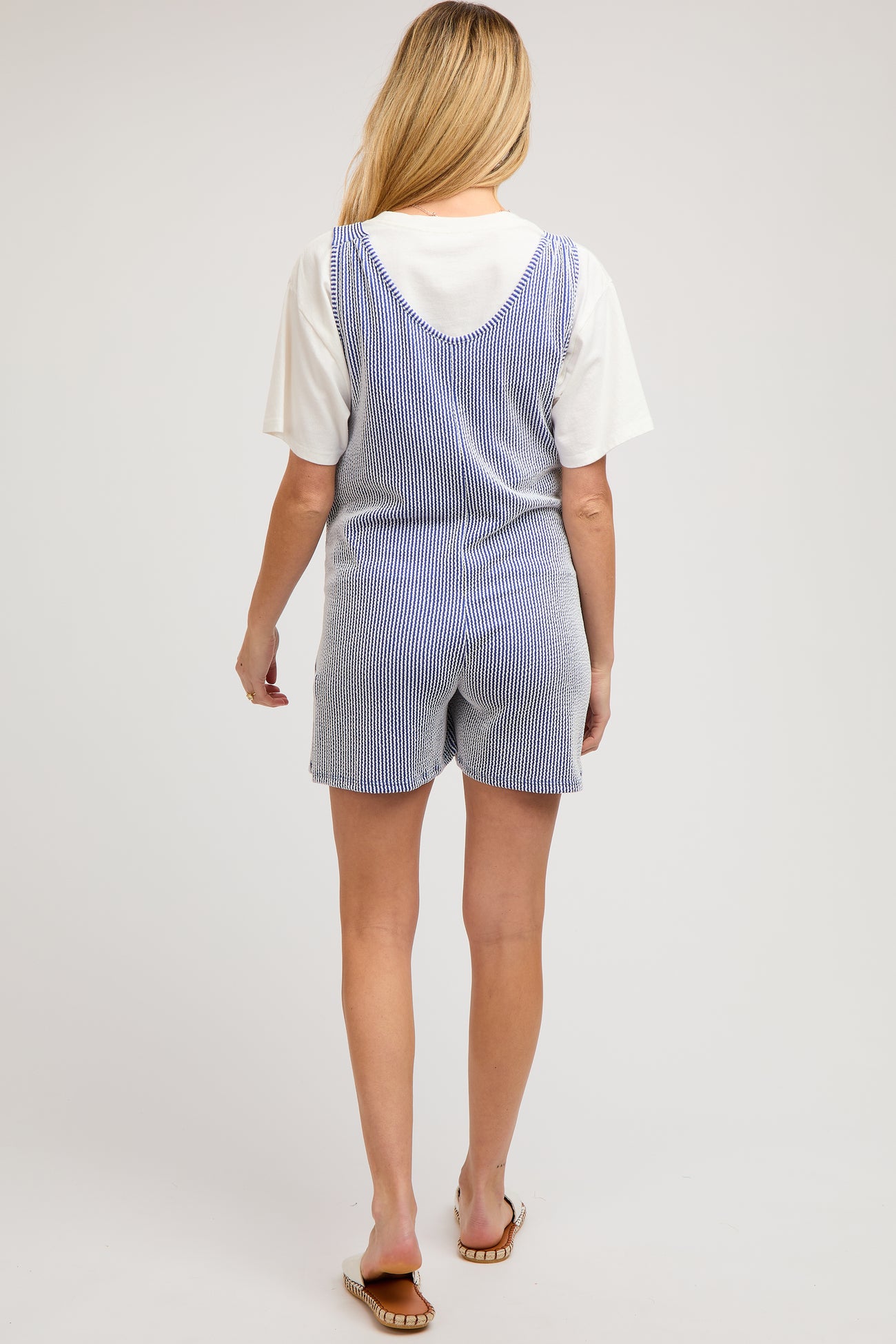 woman wearing a striped blue and white maternity romper and a white short sleeve top, view from the back