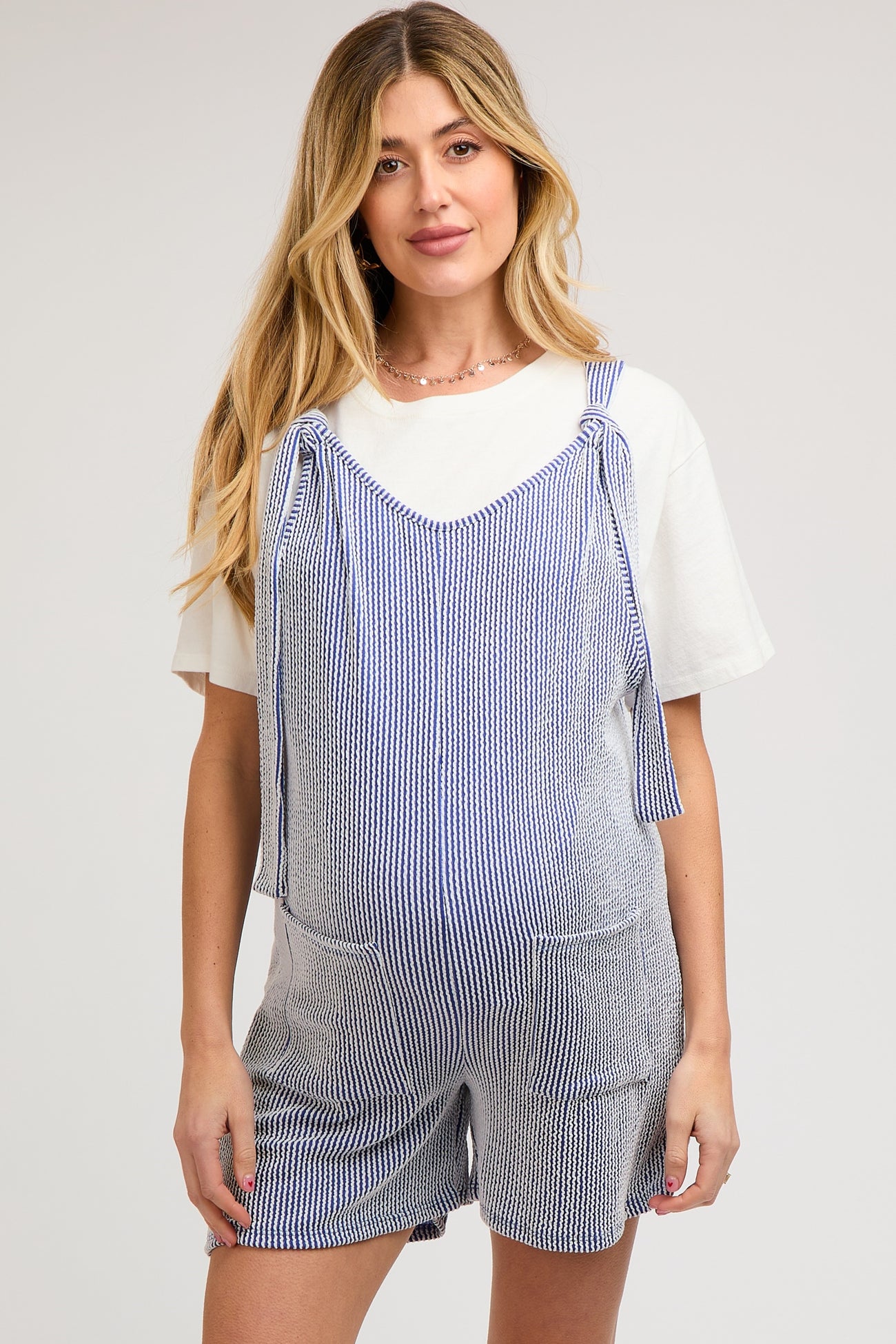 woman wearing a blue and white striped maternity romper with tie straps and pockets, showing her baby bump