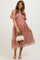 woman wearing a dusty pink maternity dress with floral embroidery and short sleeves, holding a small handbag and showing her baby bump
