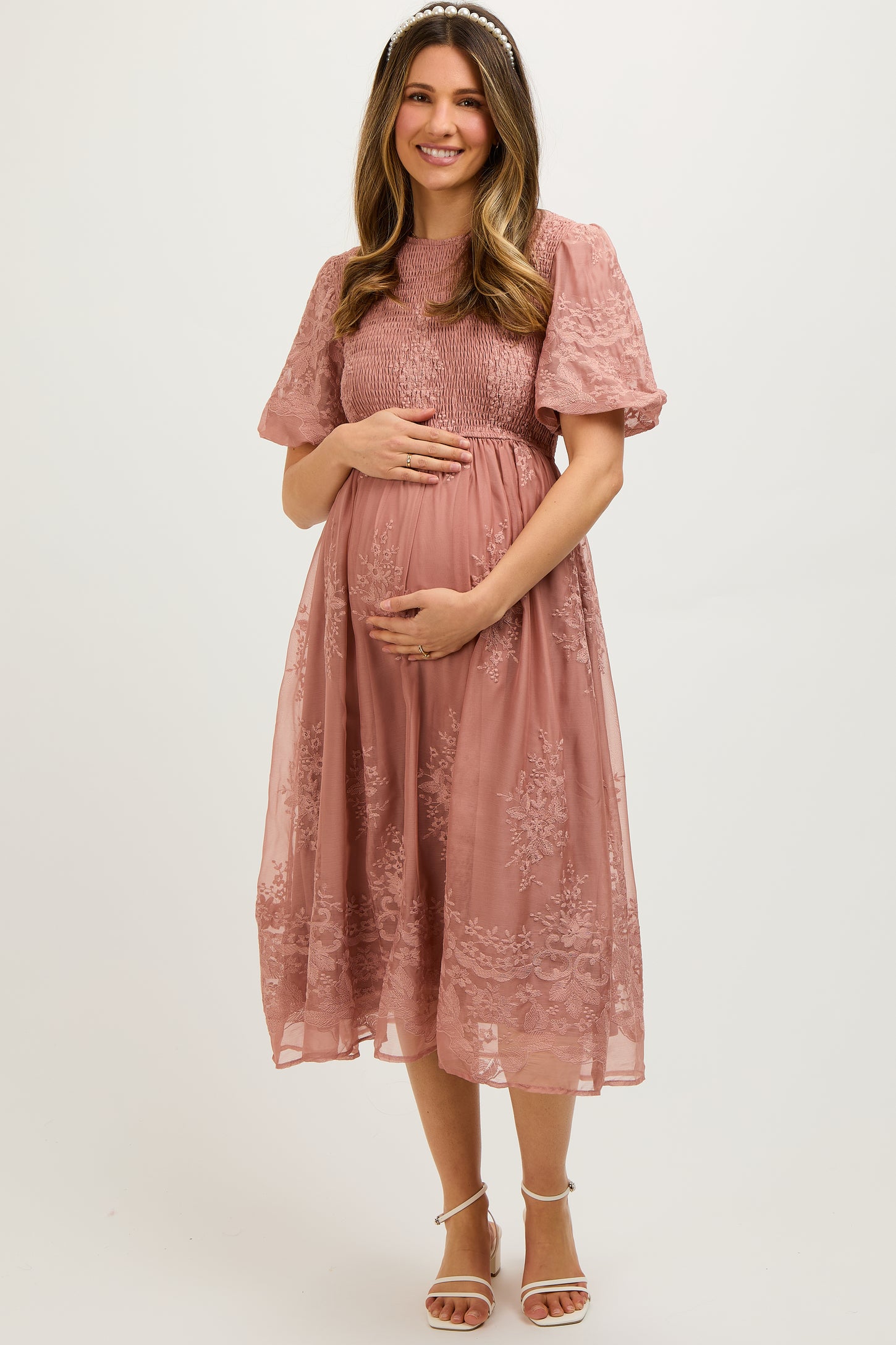 woman wearing a dusty rose maternity dress with short puff sleeves and lace details, cradling her baby bump