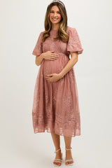 woman wearing a dusty rose maternity dress with short puff sleeves and lace details, cradling her baby bump