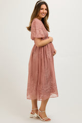 woman wearing a dusty rose maternity dress with floral embroidery and short sleeves, holding her baby bump