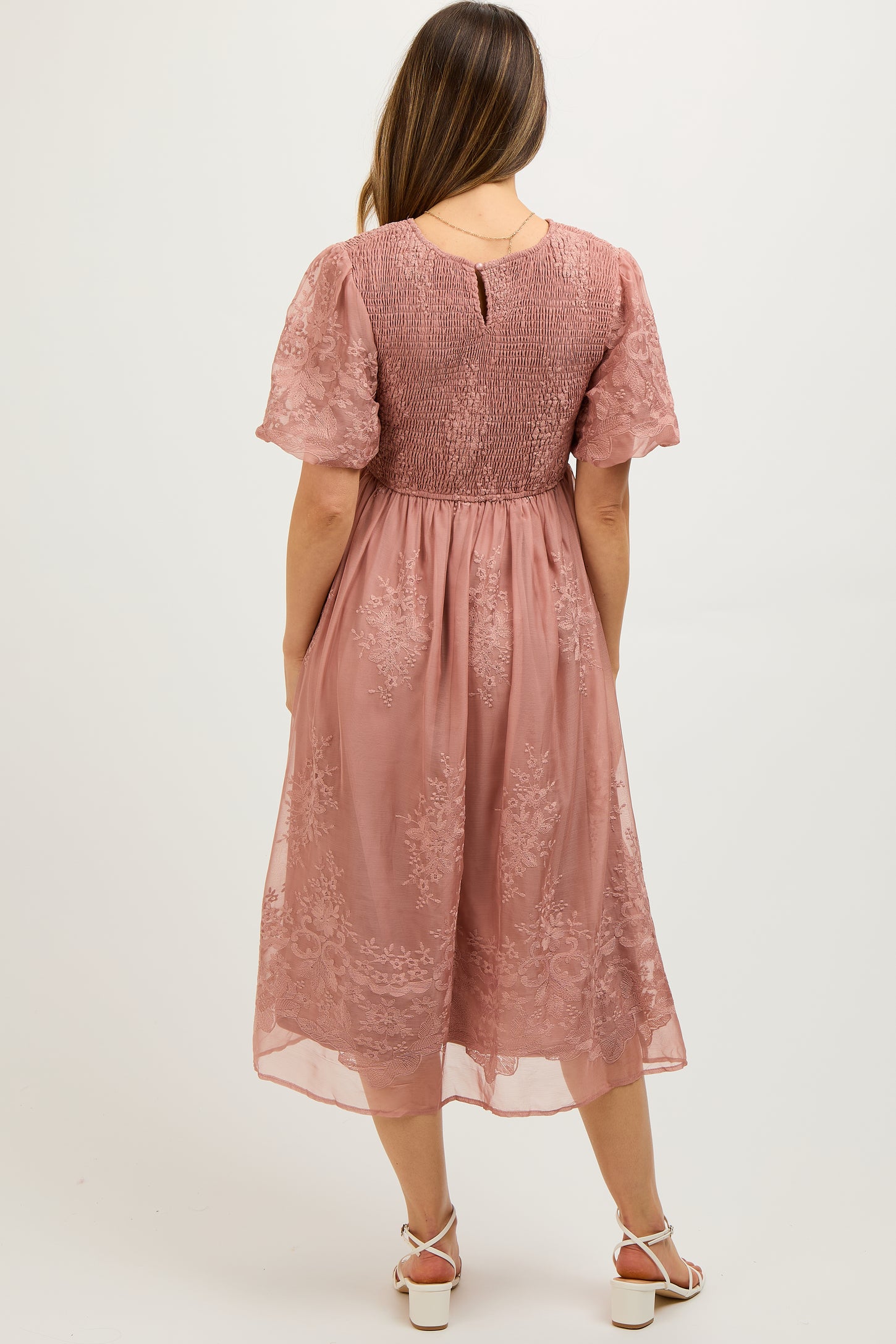 woman wearing a dusty rose maternity dress with short sleeves and floral lace details, showcasing a baby bump from the back