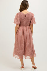 woman wearing a dusty rose maternity dress with short sleeves and floral lace details, showcasing a baby bump from the back