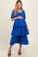 woman wearing a bright blue maternity dress with tiered layers and puff sleeves, holding her baby bump
