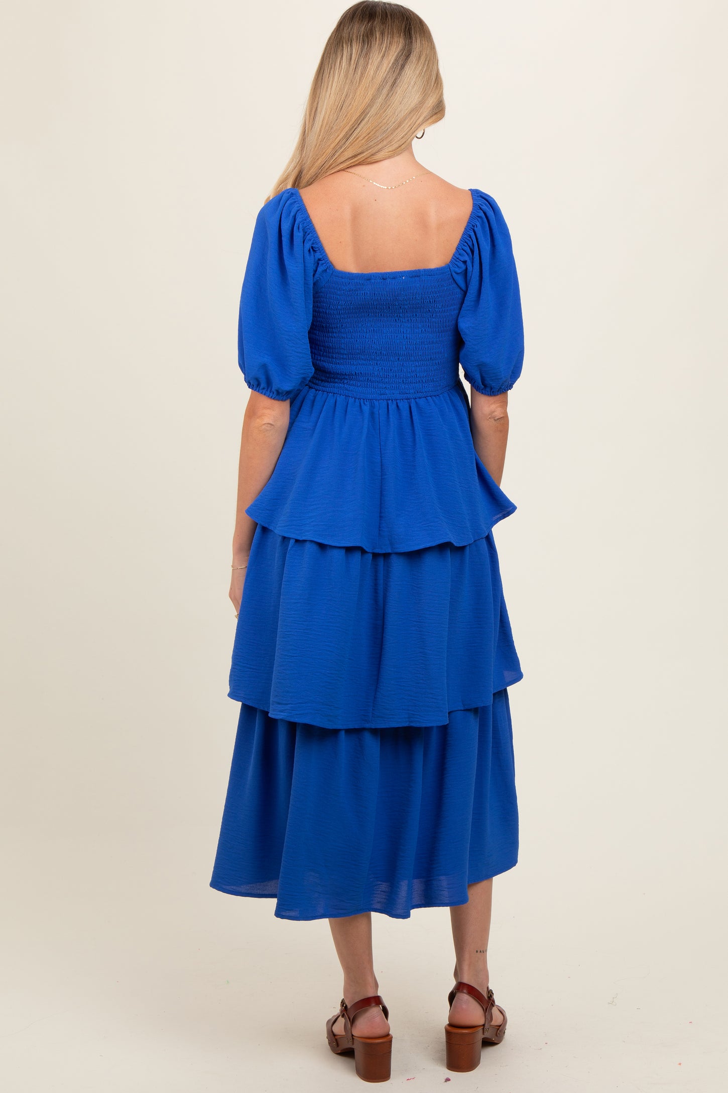 woman wearing a blue maternity dress with puff sleeves and tiered ruffles, showing a relaxed fit from the back