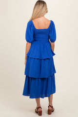 woman wearing a blue maternity dress with puff sleeves and tiered ruffles, showing a relaxed fit from the back