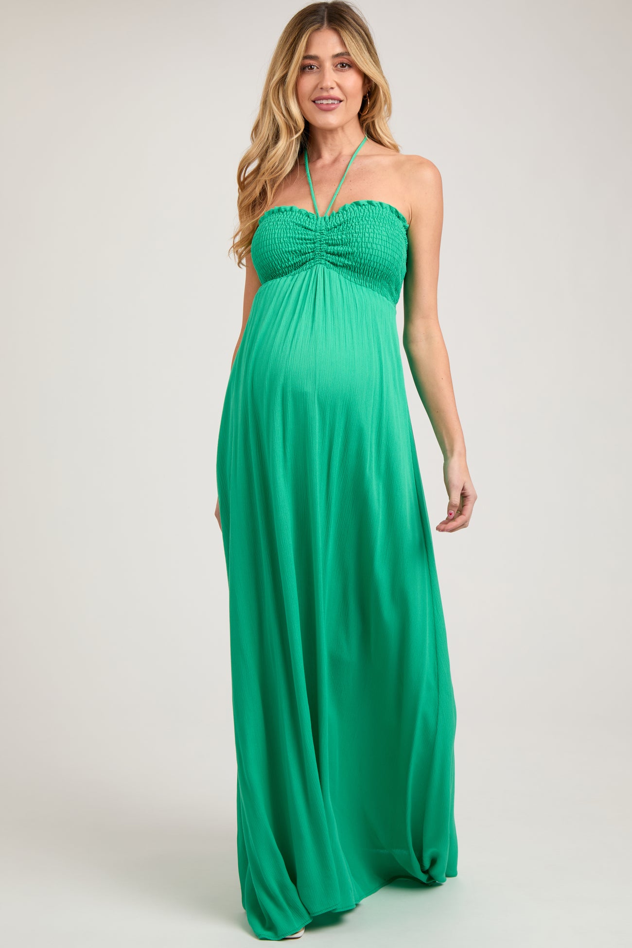 woman wearing a bright green halter neck maternity maxi dress with smocked bodice and baby bump visible