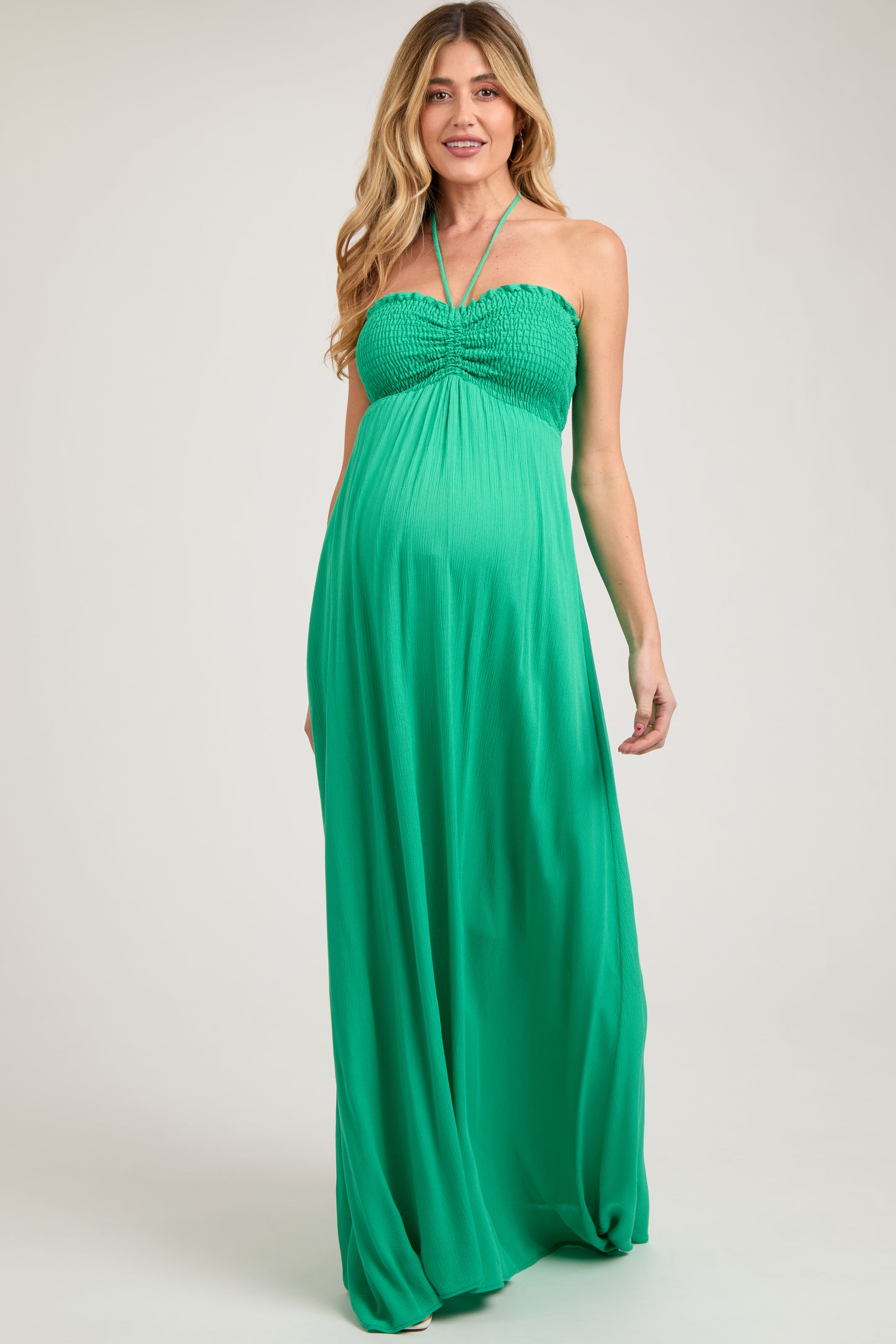 woman wearing a bright green halter neck maternity maxi dress with smocked bodice and baby bump visible