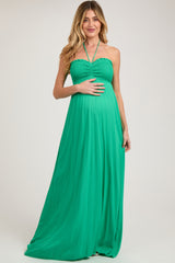 woman wearing a green halter neck maternity maxi dress and holding her baby bump