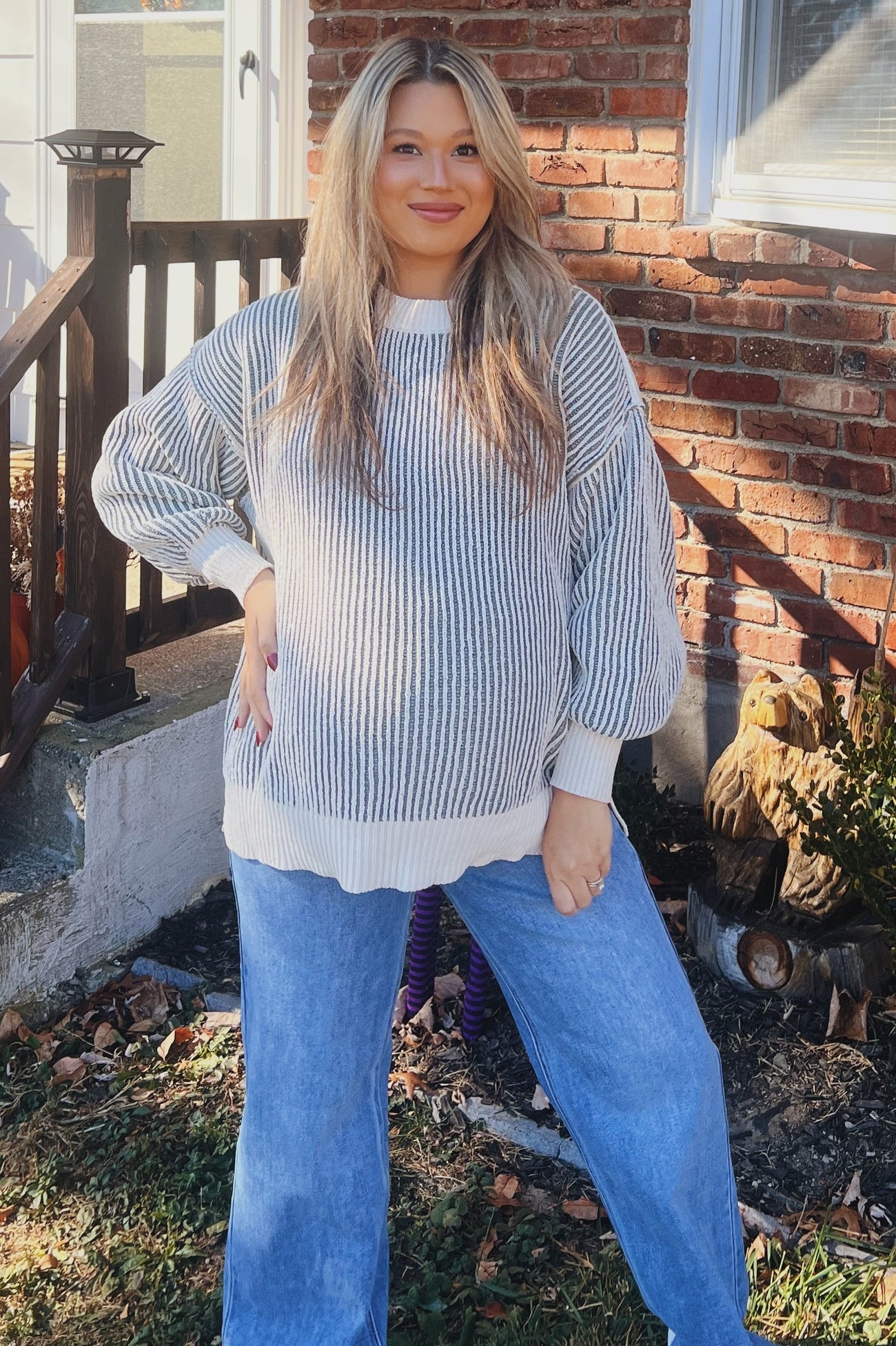 woman wearing a gray and white striped maternity sweater with a relaxed fit and blue wide-leg jeans, showing her baby bump