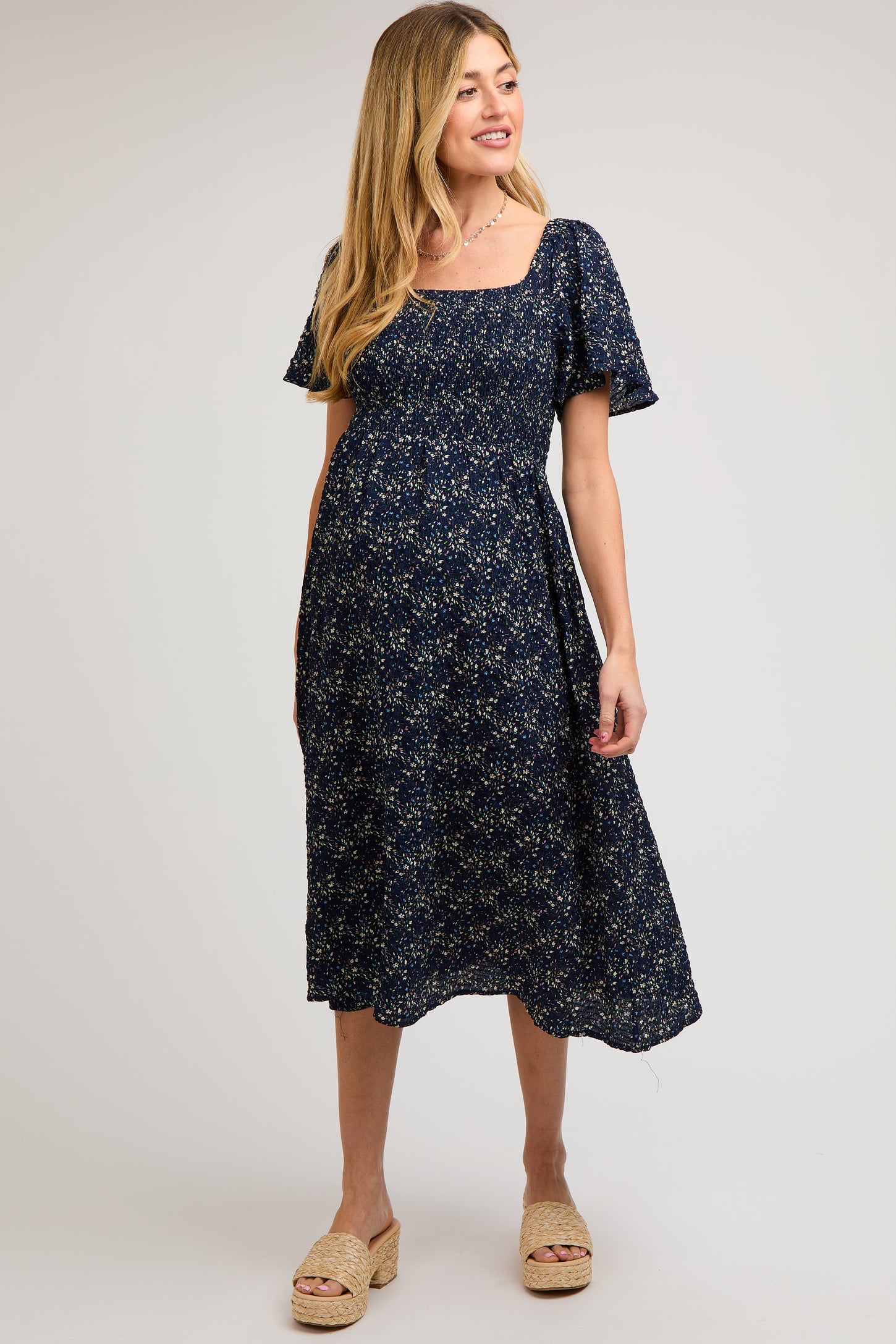 woman wearing a navy blue floral print maternity dress with a square neckline and short puff sleeves, showing her baby bump