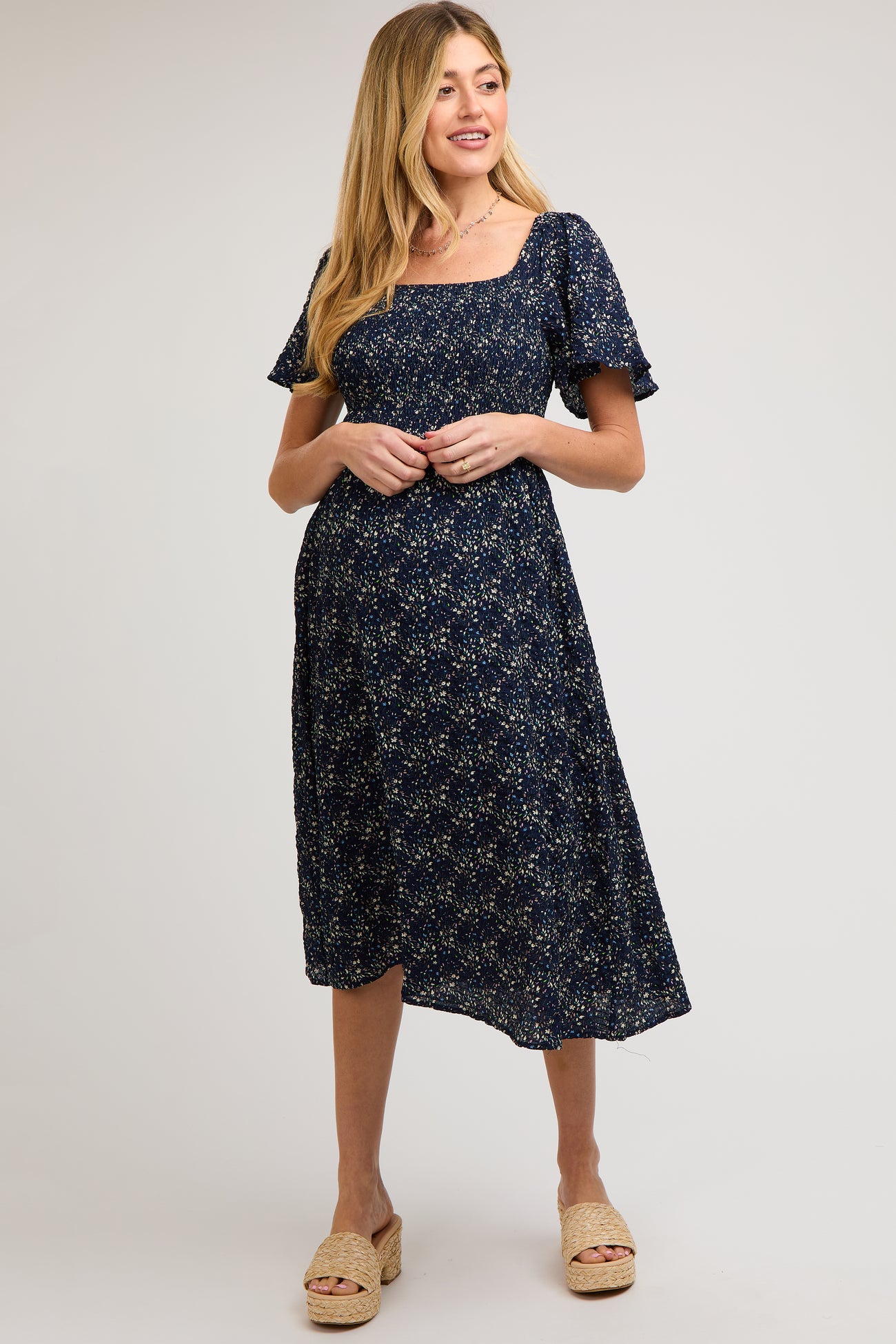 woman wearing a navy floral maternity dress with short sleeves and a square neckline, highlighting her baby bump