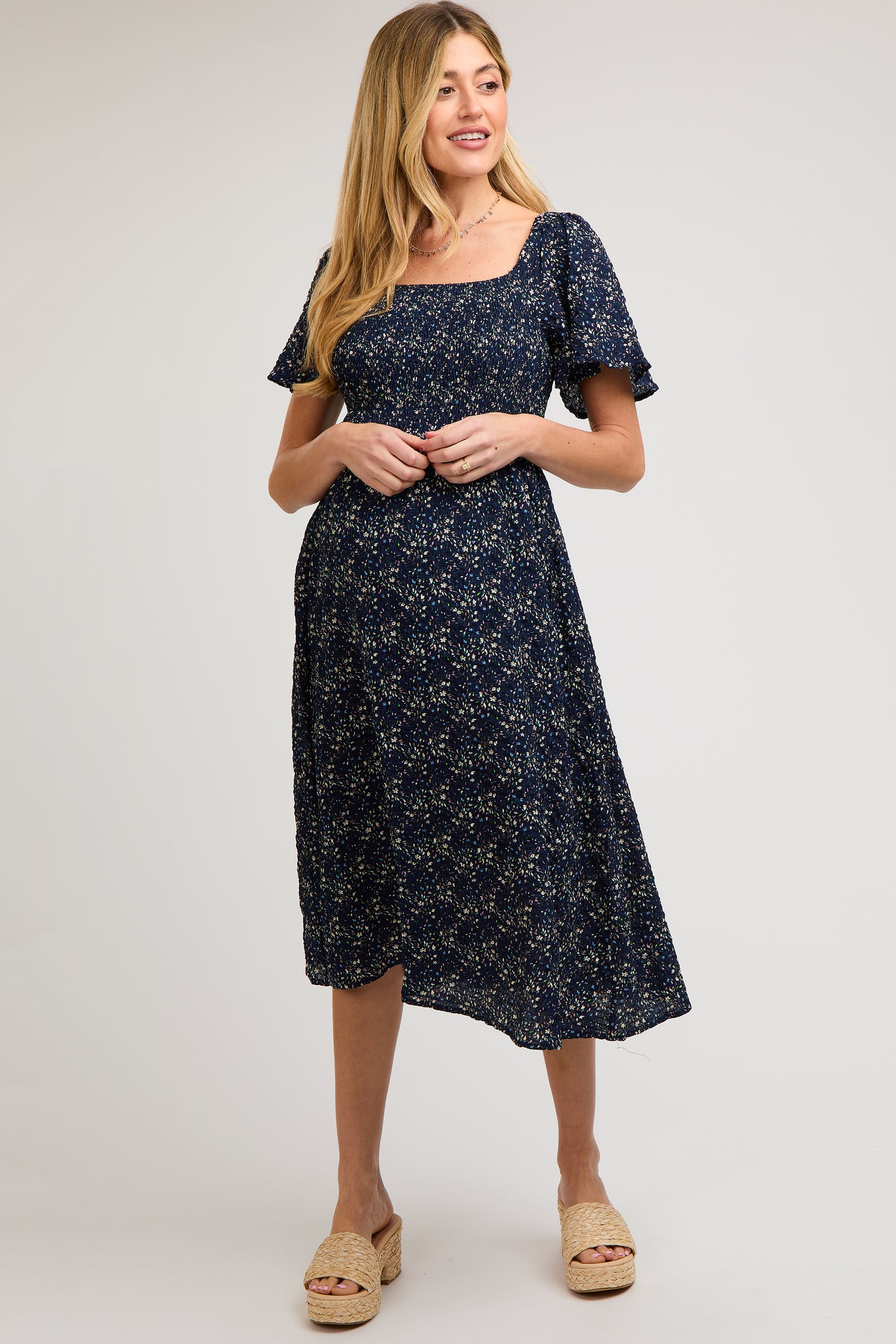 woman wearing a navy floral maternity dress with short sleeves and a square neckline, highlighting her baby bump