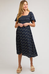 woman wearing a navy floral maternity dress with short sleeves and a square neckline, highlighting her baby bump