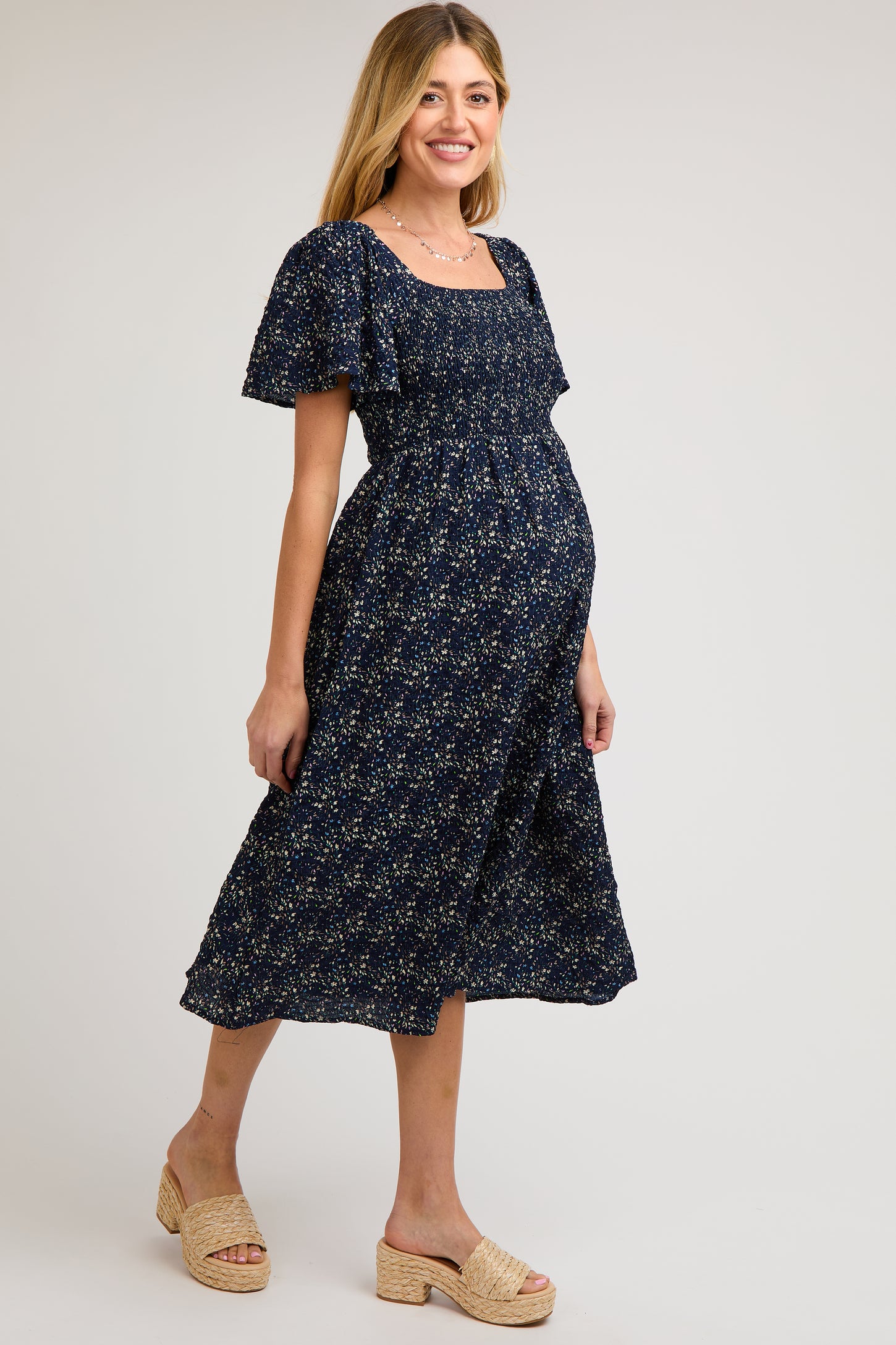 woman wearing a navy blue floral maternity dress with short sleeves and a square neckline, showcasing her baby bump