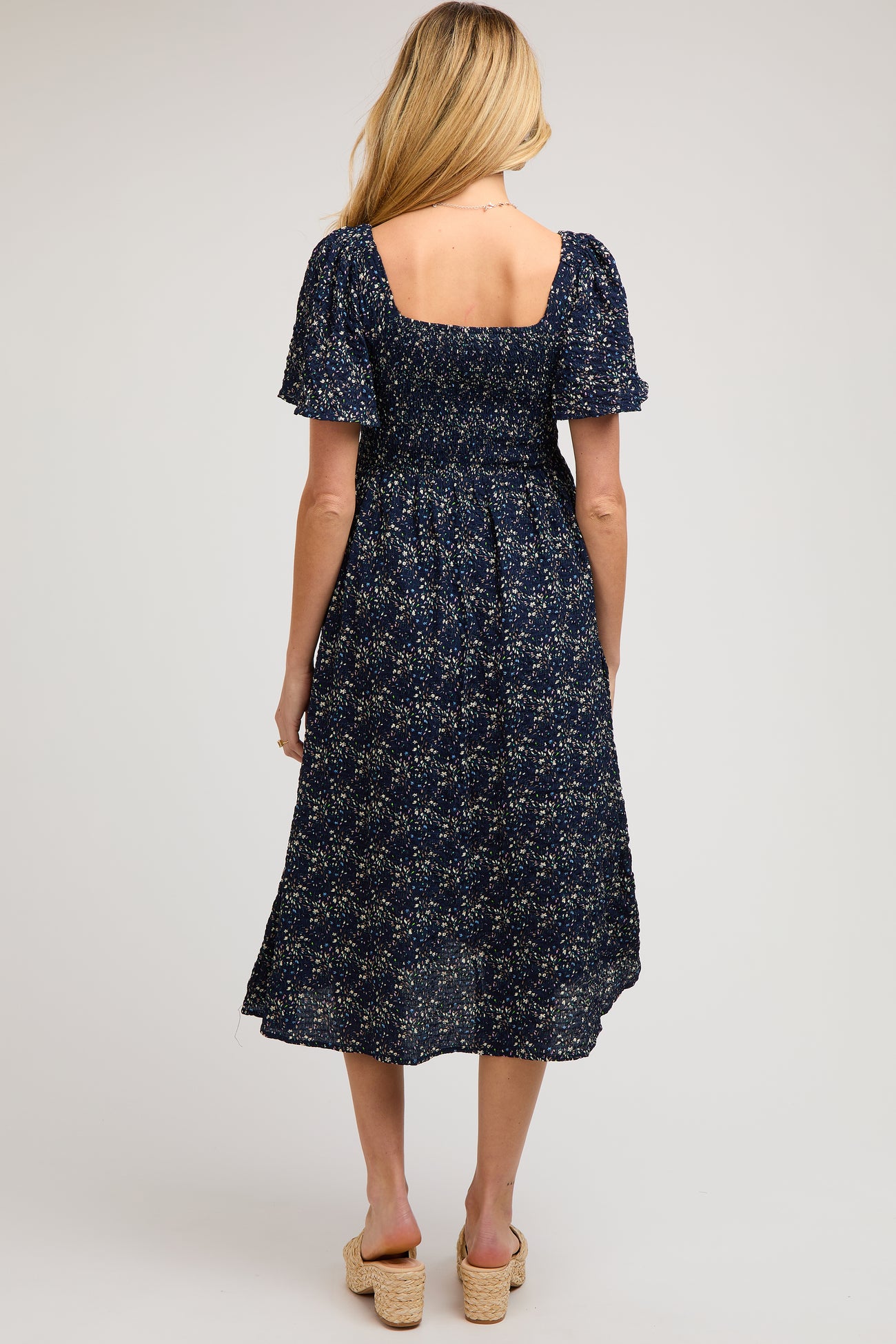 woman wearing a navy blue floral maternity dress with short puff sleeves and a smocked back, showing a baby bump
