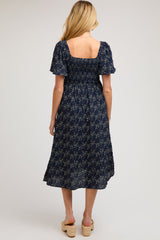 woman wearing a navy blue floral maternity dress with short puff sleeves and a smocked back, showing a baby bump
