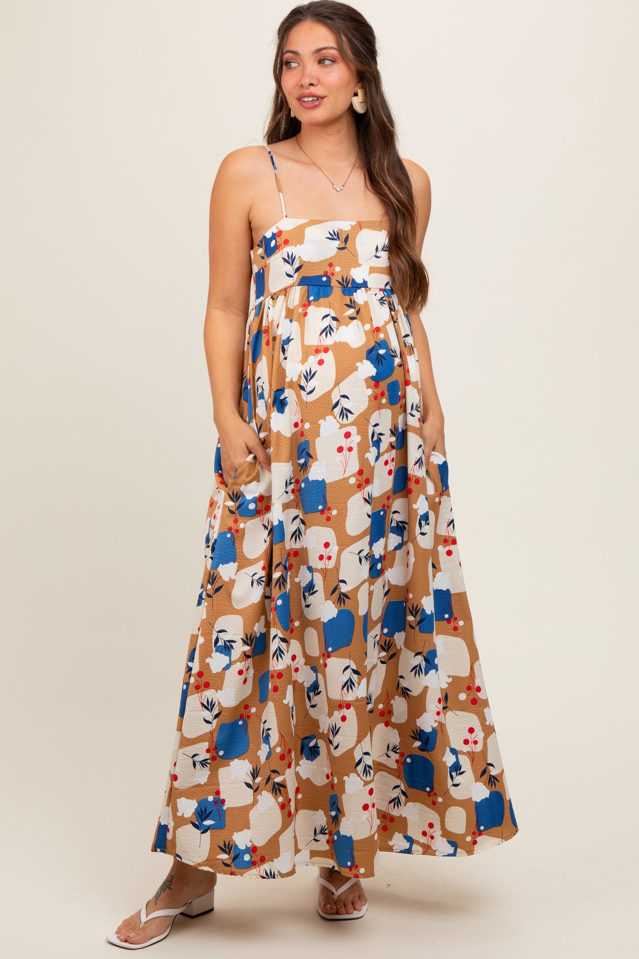 woman wearing a floral print maternity maxi dress with spaghetti straps and pockets, showcasing her baby bump
