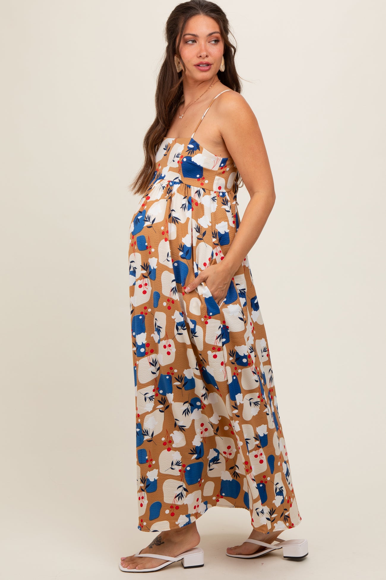 woman wearing a patterned maternity maxi dress with adjustable straps and side pockets, showcasing her baby bump