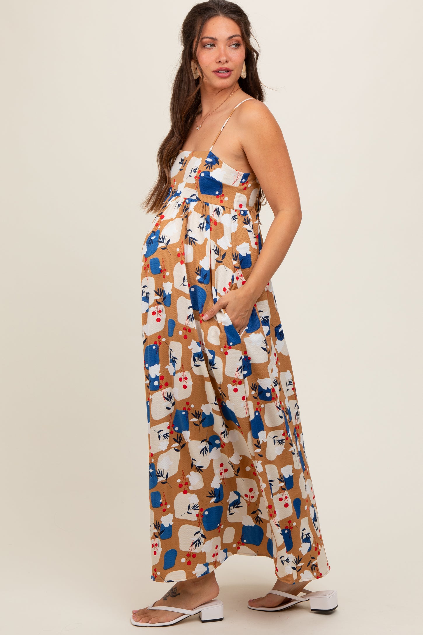 woman wearing a patterned maternity maxi dress with adjustable straps and side pockets, showcasing her baby bump