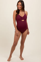 woman wearing a burgundy maternity one-piece swimsuit with a cutout detail and adjustable side ties, showcasing her baby bump