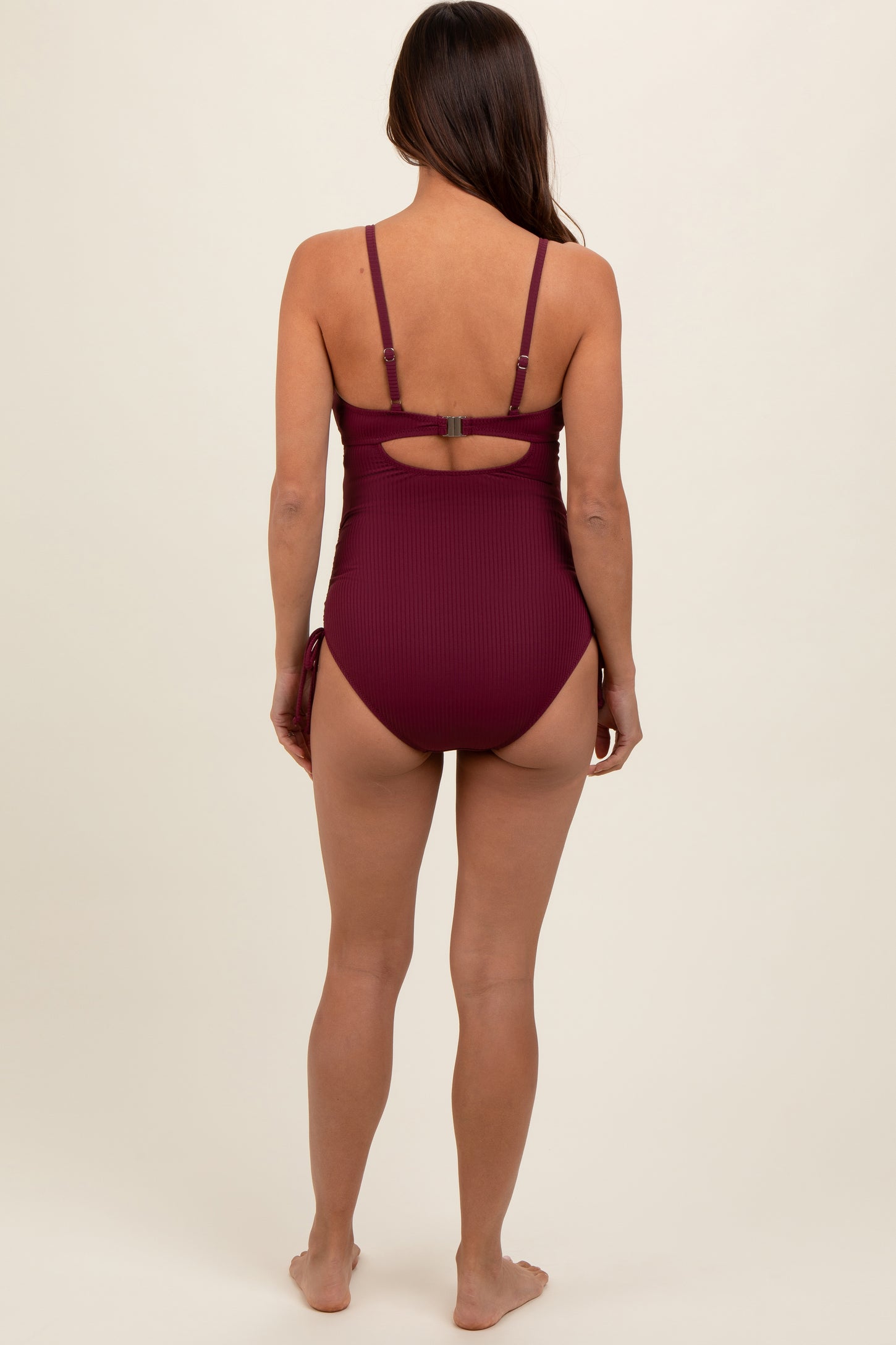 woman wearing a burgundy maternity swimsuit with adjustable straps and a cutout back, no visible baby bump