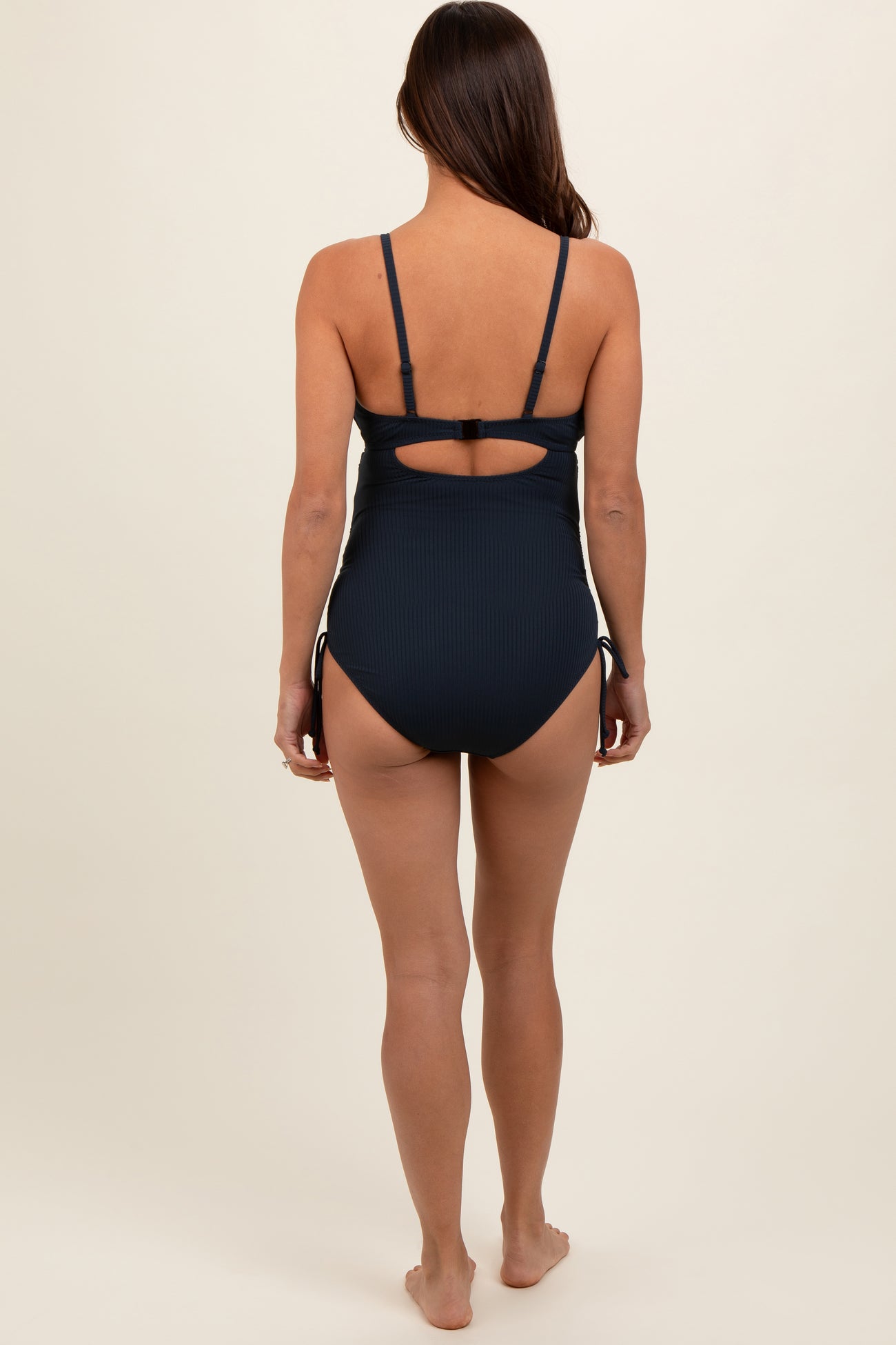 woman wearing a navy blue maternity one-piece swimsuit with adjustable side ties and a back cutout design