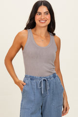 woman wearing a gray ribbed tank top and light blue drawstring pants, smiling with her hands in her pockets