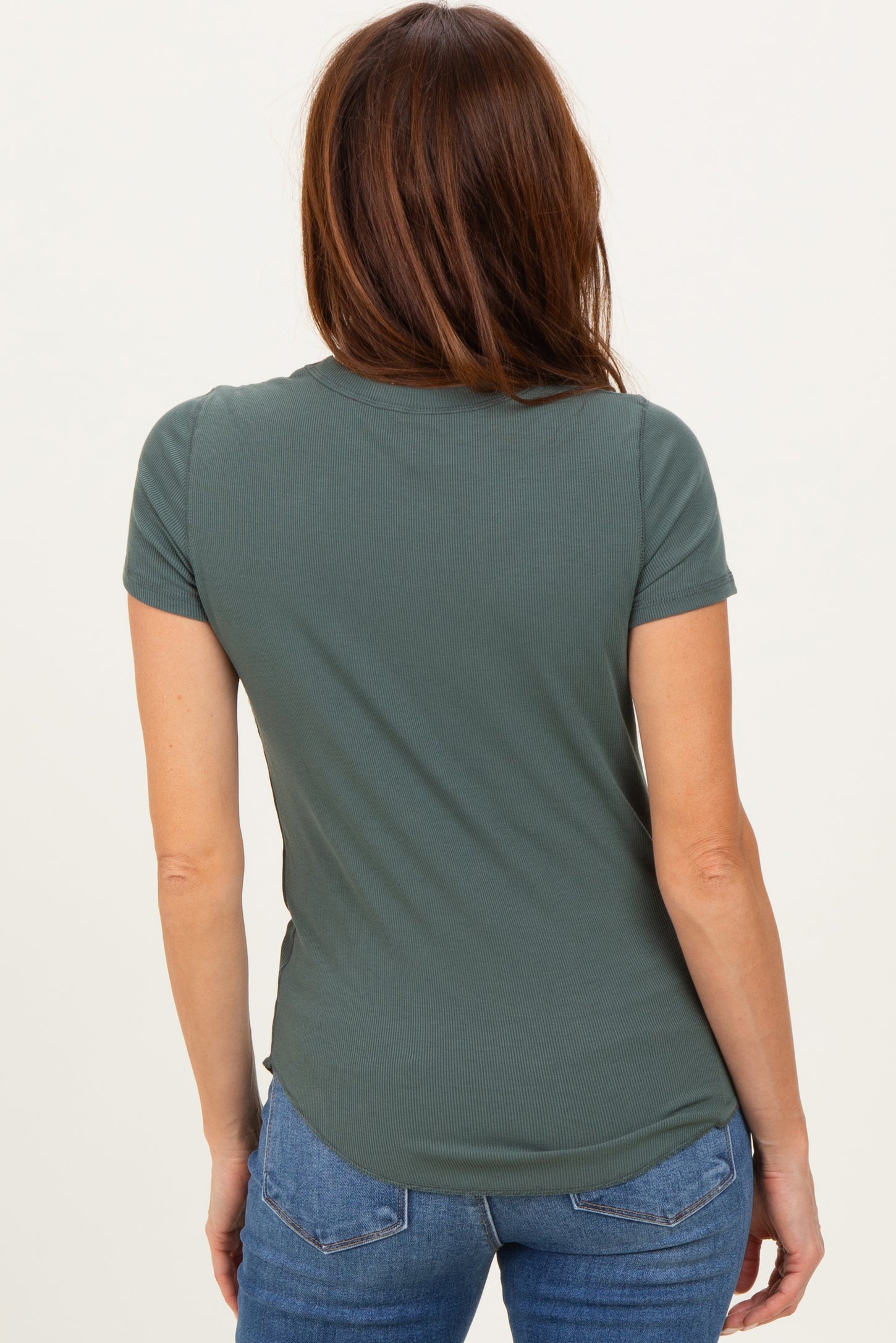 woman wearing a dark green short sleeve fitted top with a curved hem and styling with jeans