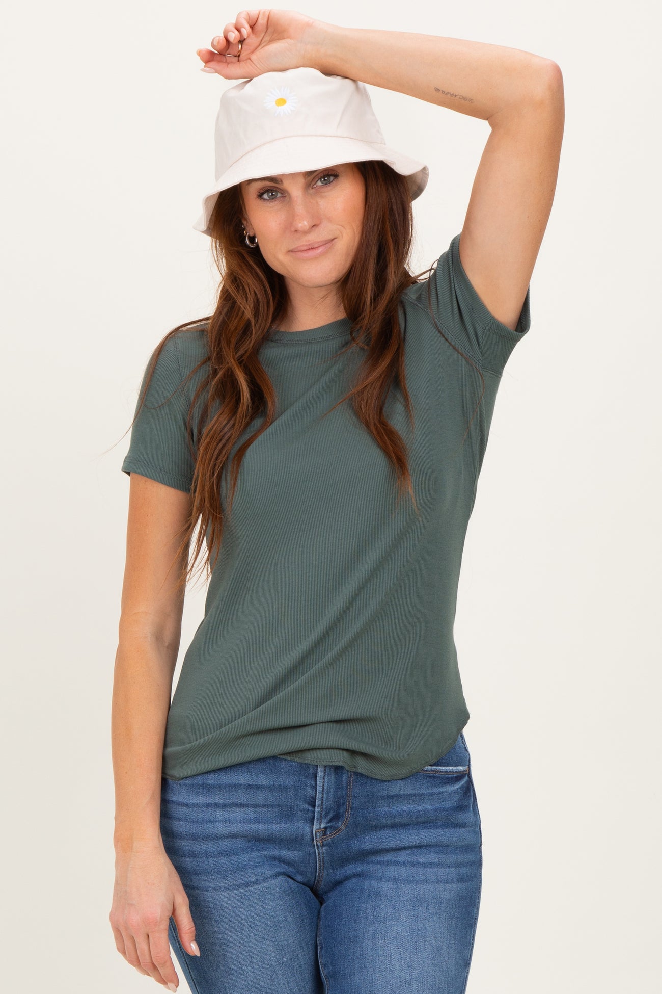 woman wearing a green short sleeve ribbed top and a white bucket hat, styled with blue jeans