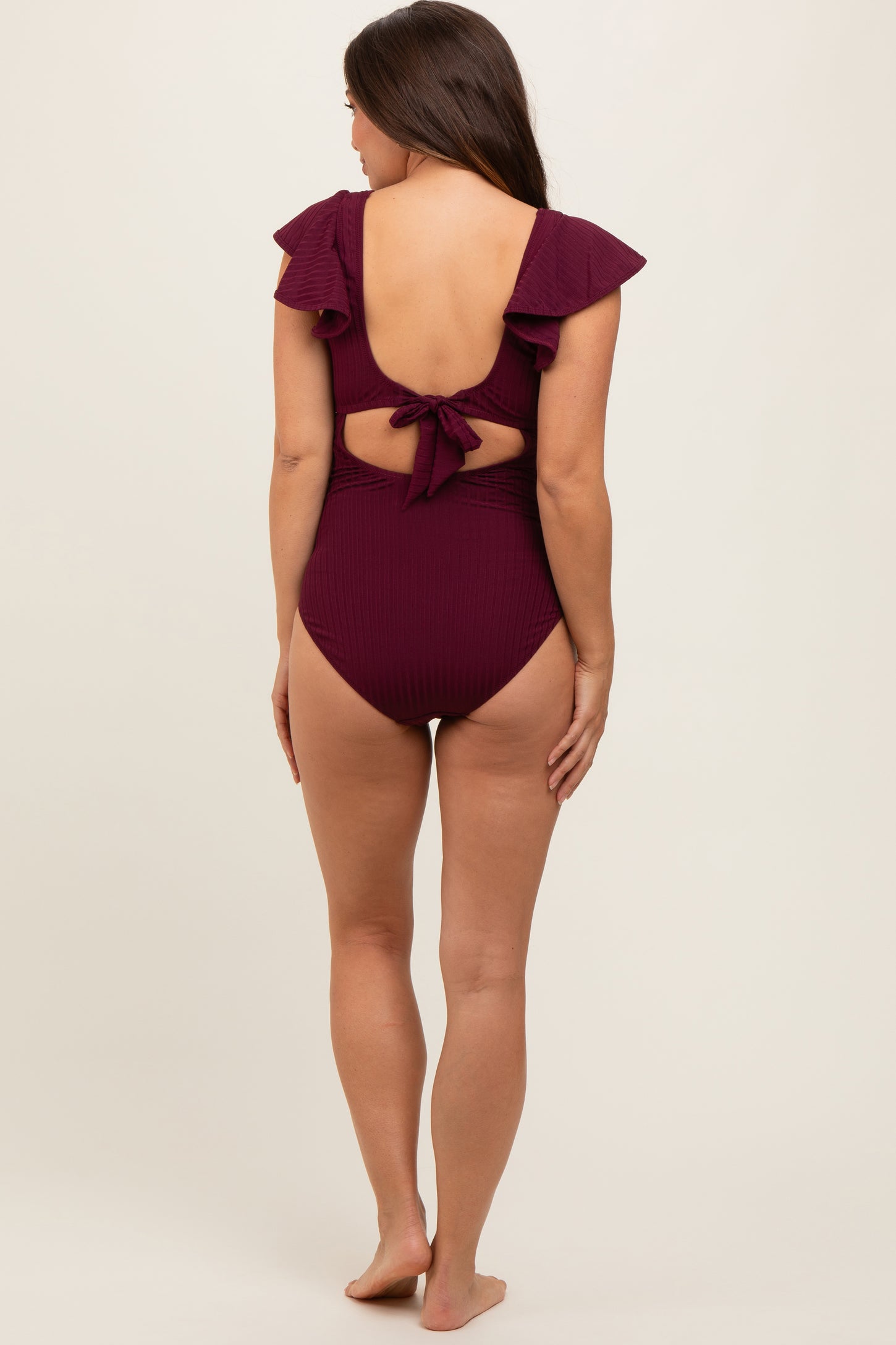 woman wearing a maroon maternity one-piece swimsuit with ruffle details and a tied back, showcasing a baby bump