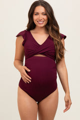 woman wearing a burgundy maternity swimsuit with flutter sleeves and a wrap design, showing her baby bump
