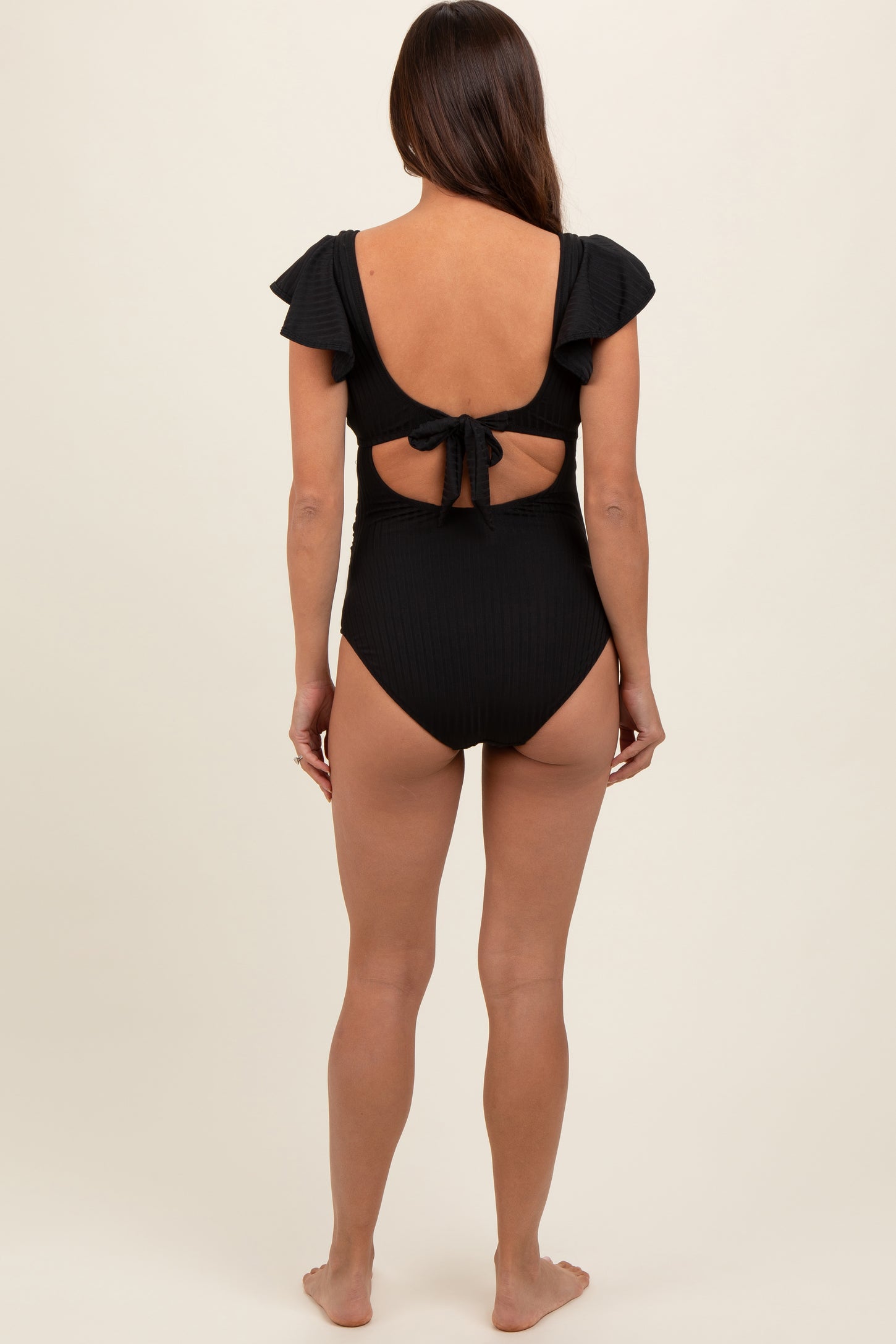 woman wearing a black maternity swimsuit with ruffle sleeves and a tie back design, showing her baby bump