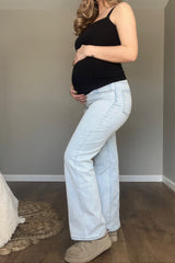 woman wearing a black tank top and light wash maternity jeans, showing her baby bump while posing sideways