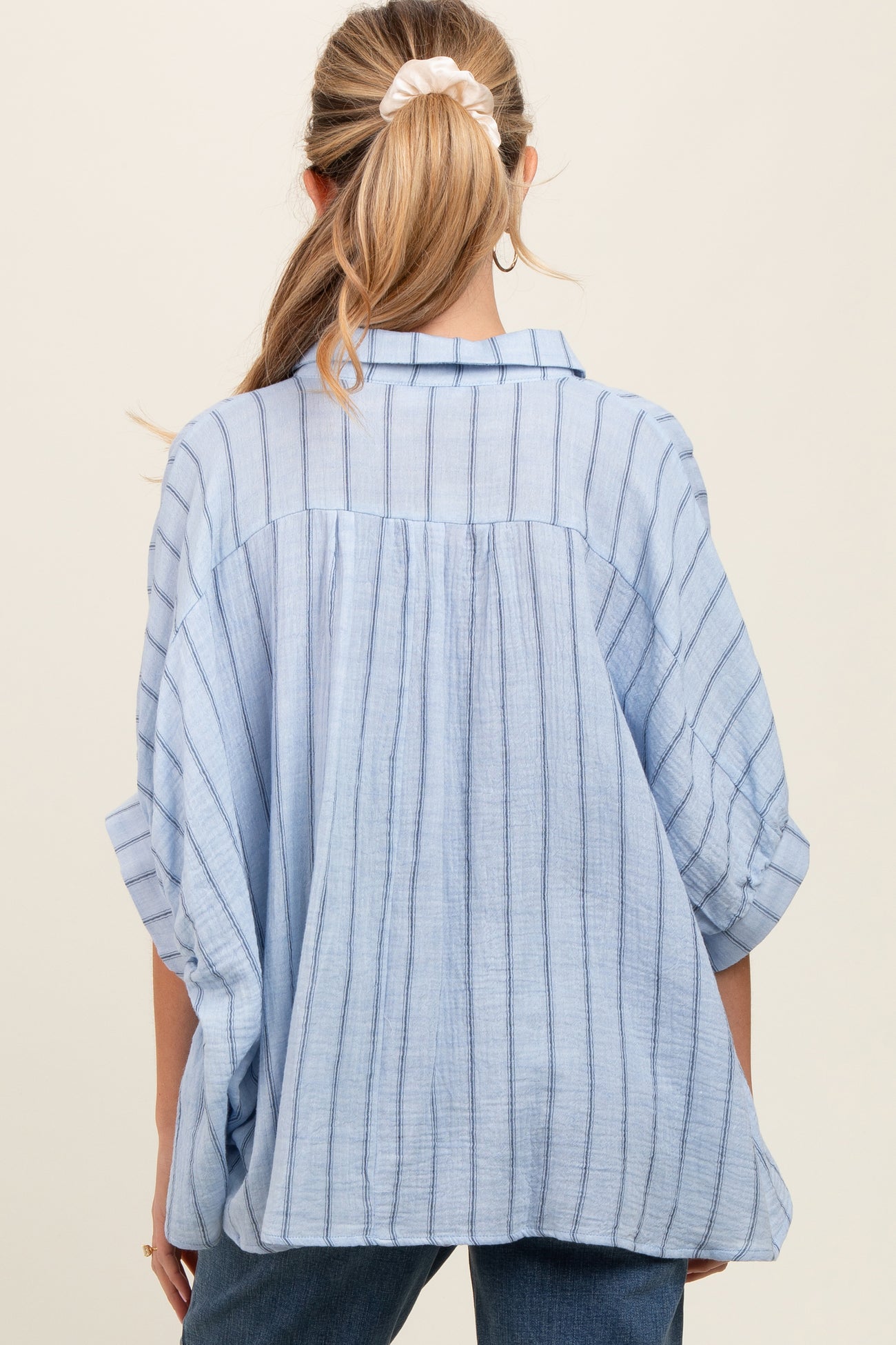 woman wearing a light blue striped maternity top with a loose fit and rolled-up sleeves, viewed from the back