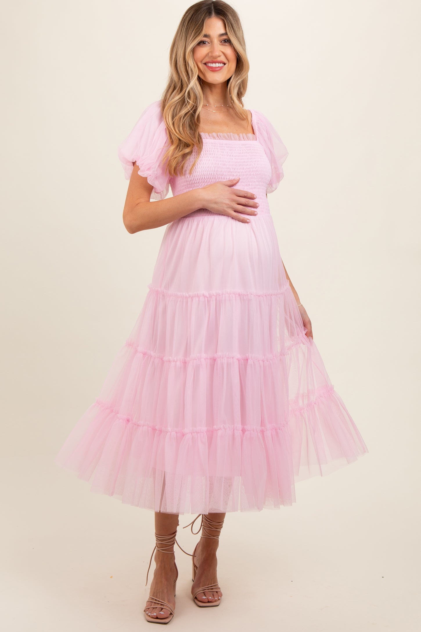 woman wearing a light pink tiered tulle maternity dress and holding her baby bump