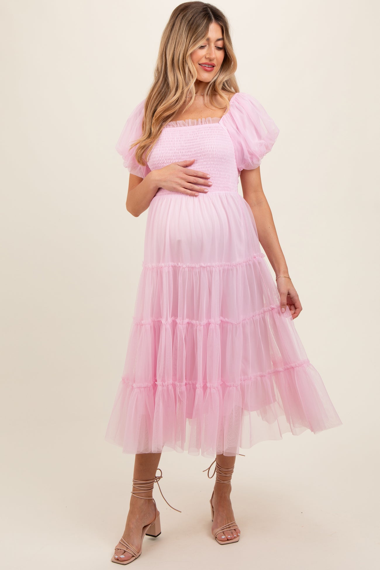 woman wearing a pink puff sleeve maternity dress with a tiered tulle skirt and holding her baby bump