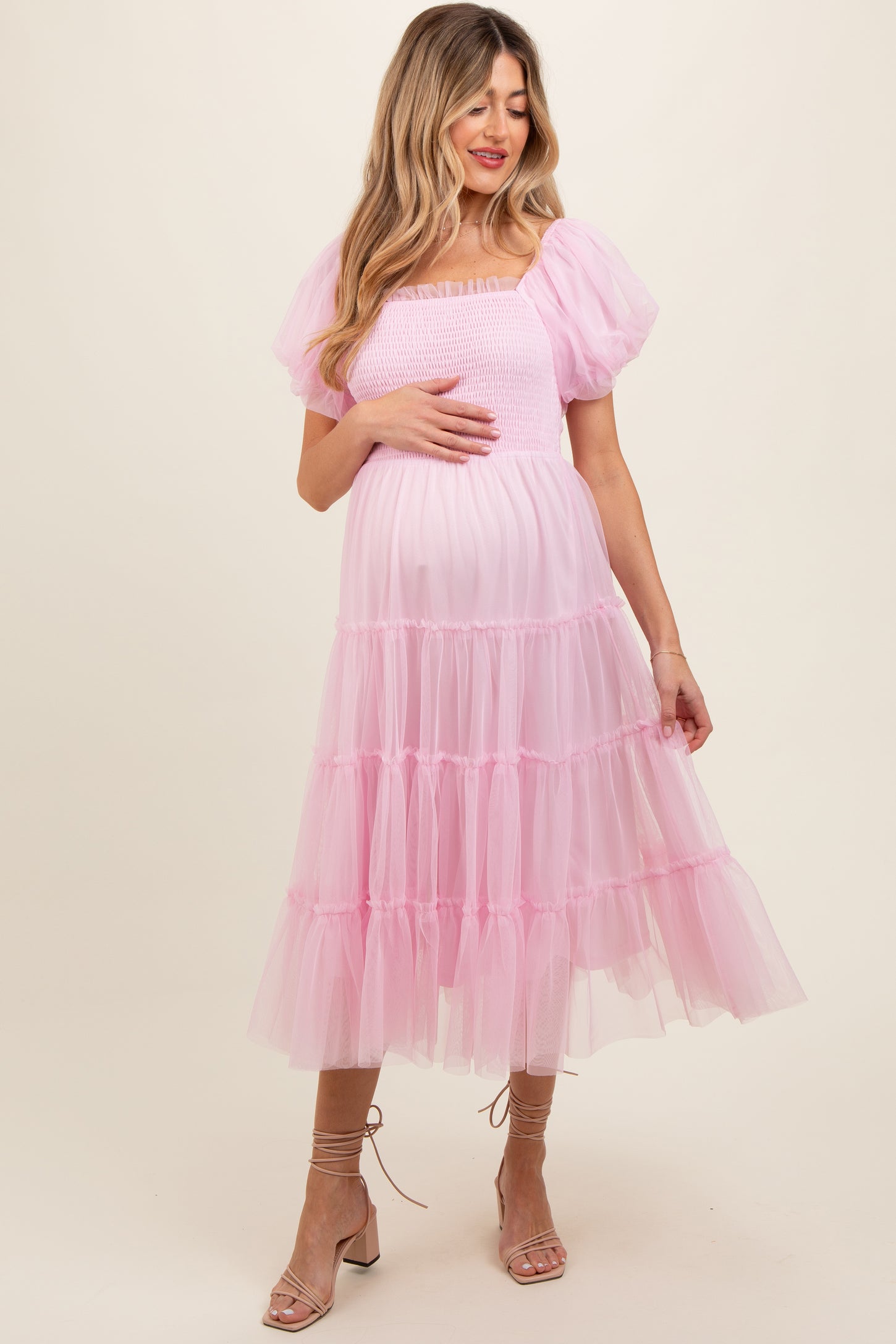 woman wearing a pink puff sleeve maternity dress with a tiered tulle skirt and holding her baby bump