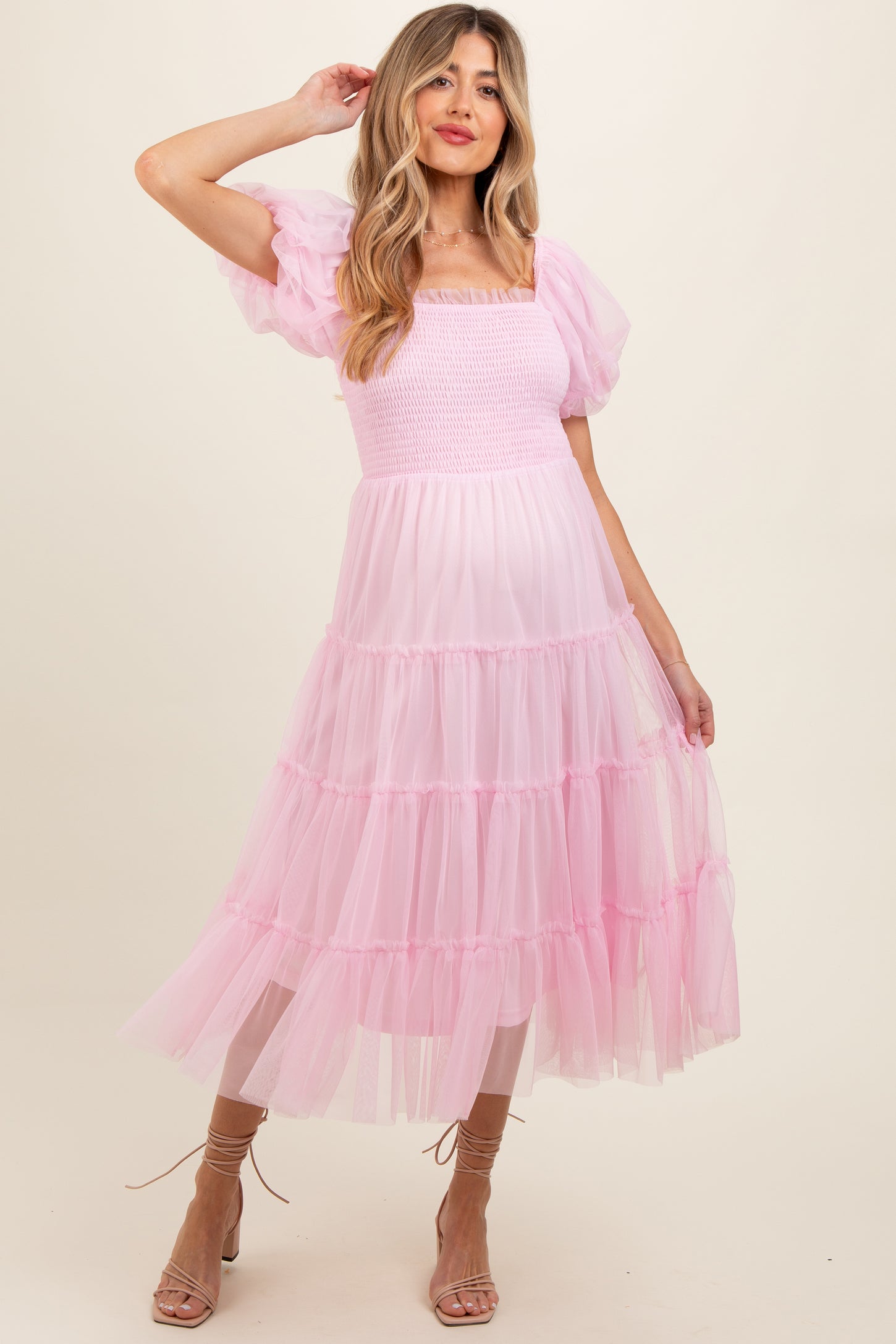 woman wearing a pink tiered tulle maternity dress with puff sleeves and a smocked bodice, showcasing her baby bump